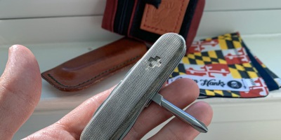 Shows the dedicated Philips head screwdriver on the Victorinox Tinker with olive drab green micarta scales in the foreground with EDC gear in the background